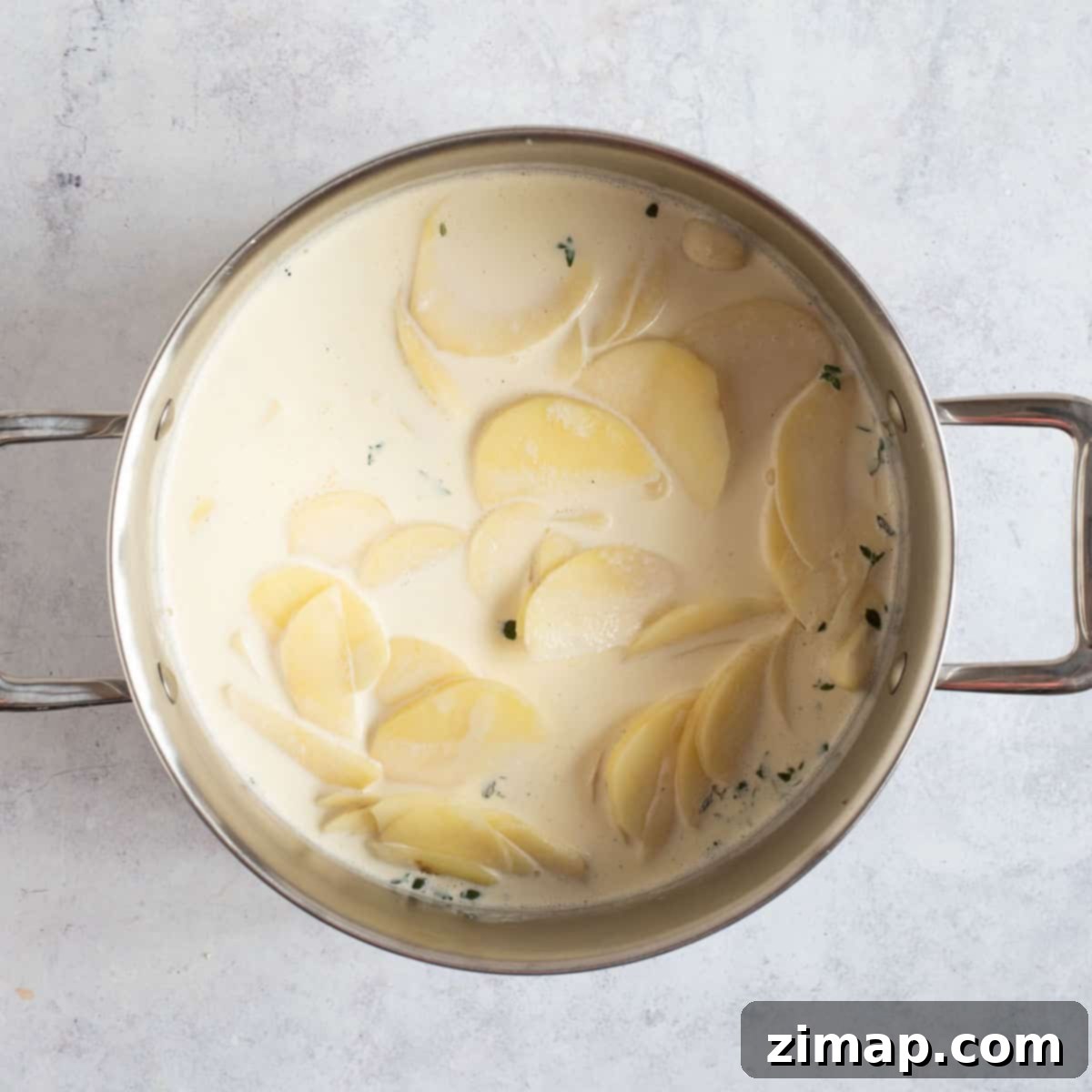 Εύκολες Πατάτες Ντοφινουά 5 Sliced potatoes in a pan with milk and cream.