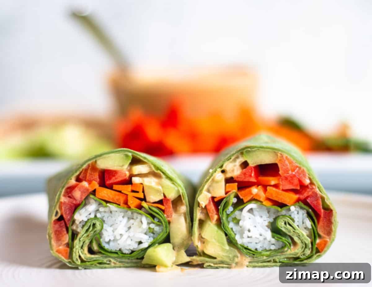 Ταϊλανδέζικα Τυλιχτά Κοτόπουλου 2 Ένα wrap σπανάκι κομμένο στη μέση σε ένα πιάτο, γεμάτο με φρέσκα λαχανικά, κοτόπουλο, noodles ρυζιού και σάλτσα φυστικοβούτυρο.