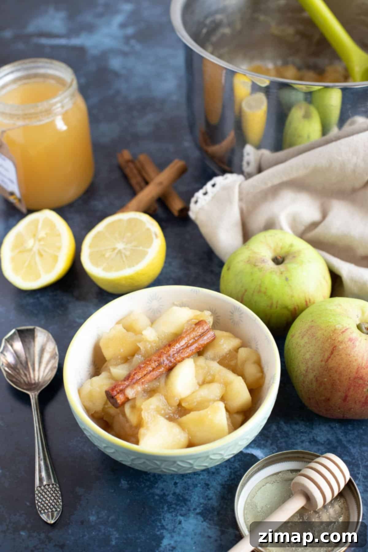 Εύκολη Κομπόστα Μήλου με Κανέλα 2 Stewed apples in a bowl with a pan of stewed apples behind.