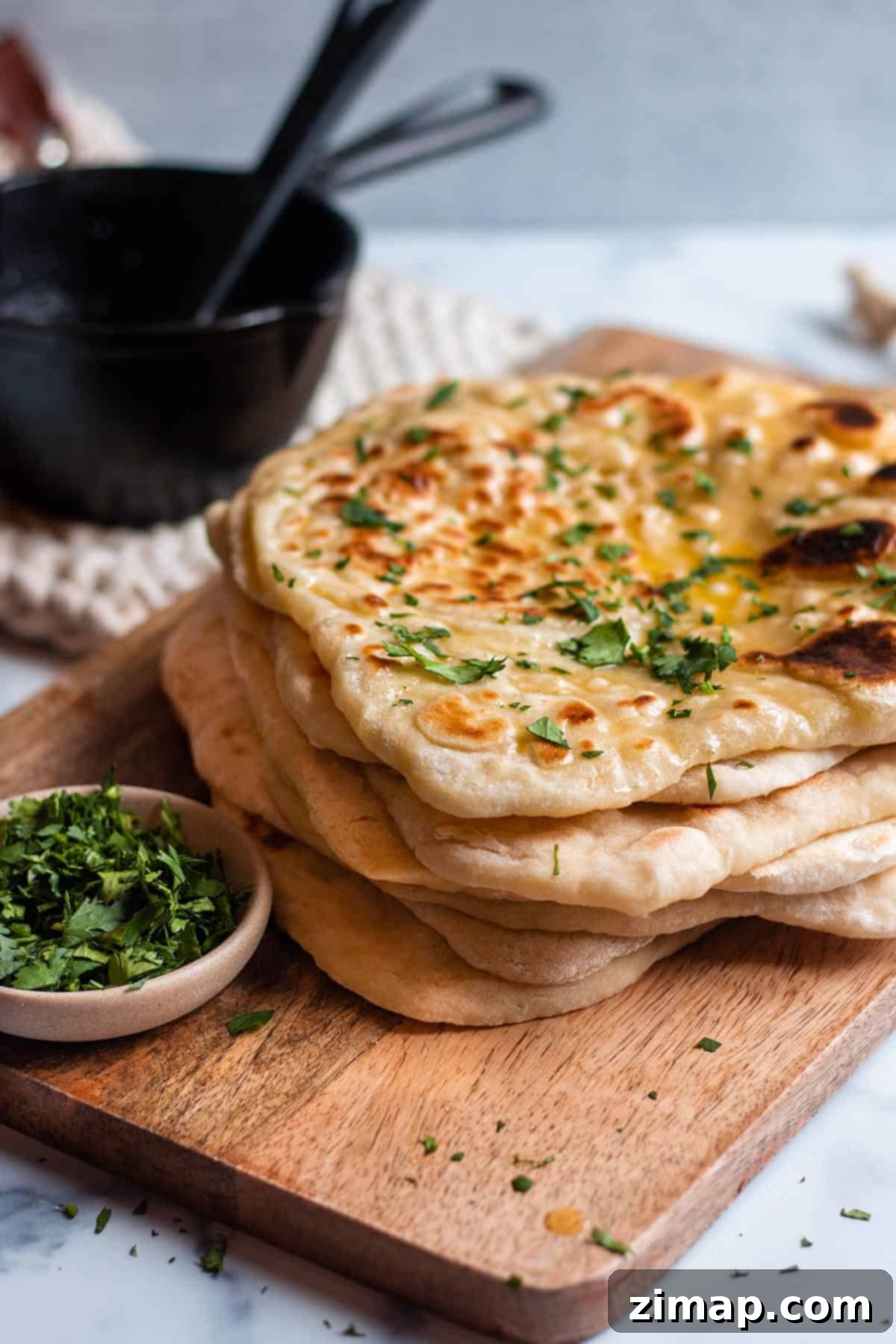 Προζυμένιο Νάαν με περίσσευμα 2 Μια στοίβα από naan με προζύμι σε ξύλινο δίσκο με κόλιανδρο και λιωμένο βούτυρο. Μπολ με φρέσκο κόλιανδρο και μαντεμένιο δοχείο για βούτυρο.
