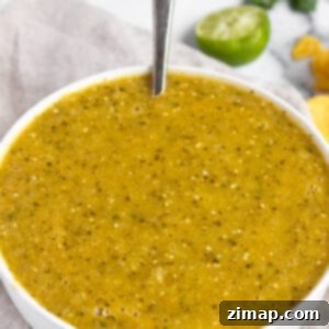 Ψητή Σάλτσα Φυσάλιδας 7 Ένα λευκό μπολ με πράσινη σάλτσα, λάιμ και τσιπς στο βάθος.