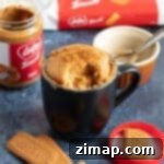 Το Απόλυτο Biscoff Κέικ Κούπας 6 Biscoff mug cake σε μια μεγάλη μαύρη κούπα πασπαλισμένο με θρυμματισμένα μπισκότα lotus.