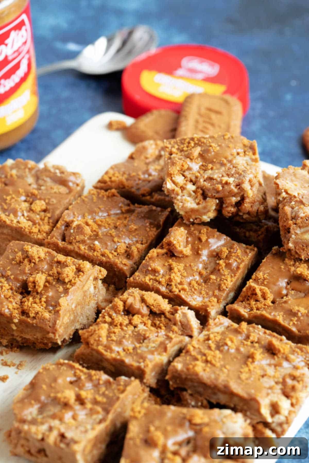 Εύκολο Τίφιν Μπισκόφ 5 Μπάρες Biscoff tiffin με ένα βάζο κρέμας Biscoff στο βάθος.