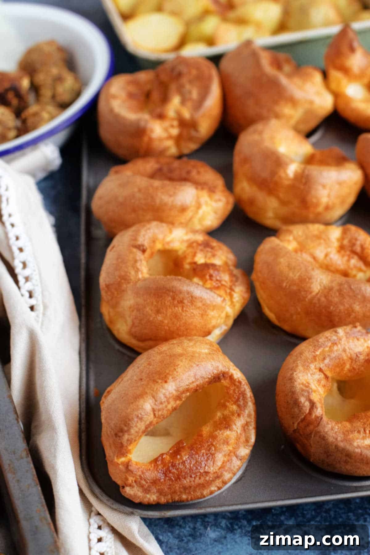 Ένα ταψί γεμάτο Yorkshire puddings με ψητές πατάτες στο παρασκήνιο.