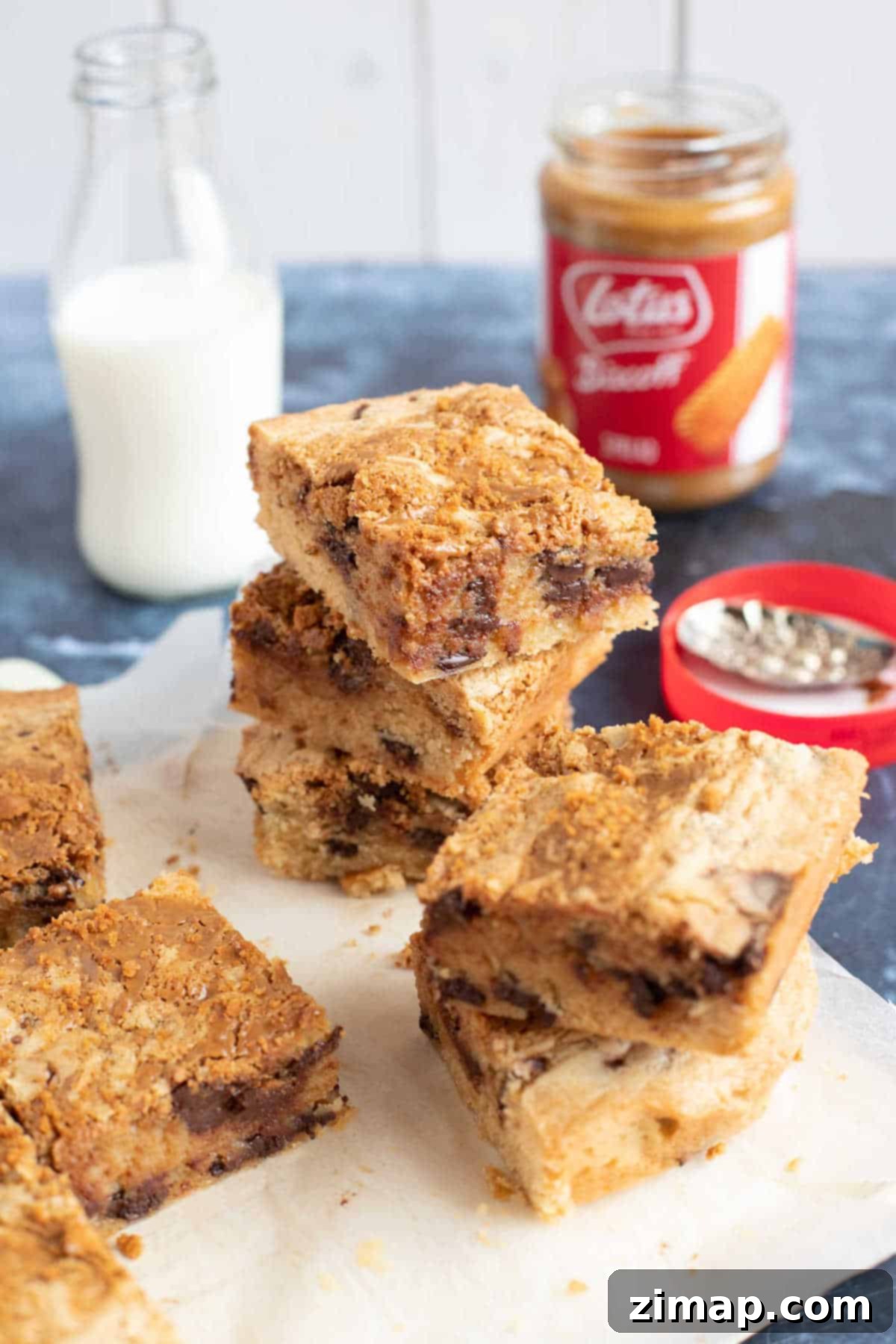 Πανεύκολα Μπλόντις Μπισκόφ 6 Κομμένα blondies σε ξύλινη επιφάνεια με ένα ποτήρι γάλα στο βάθος.