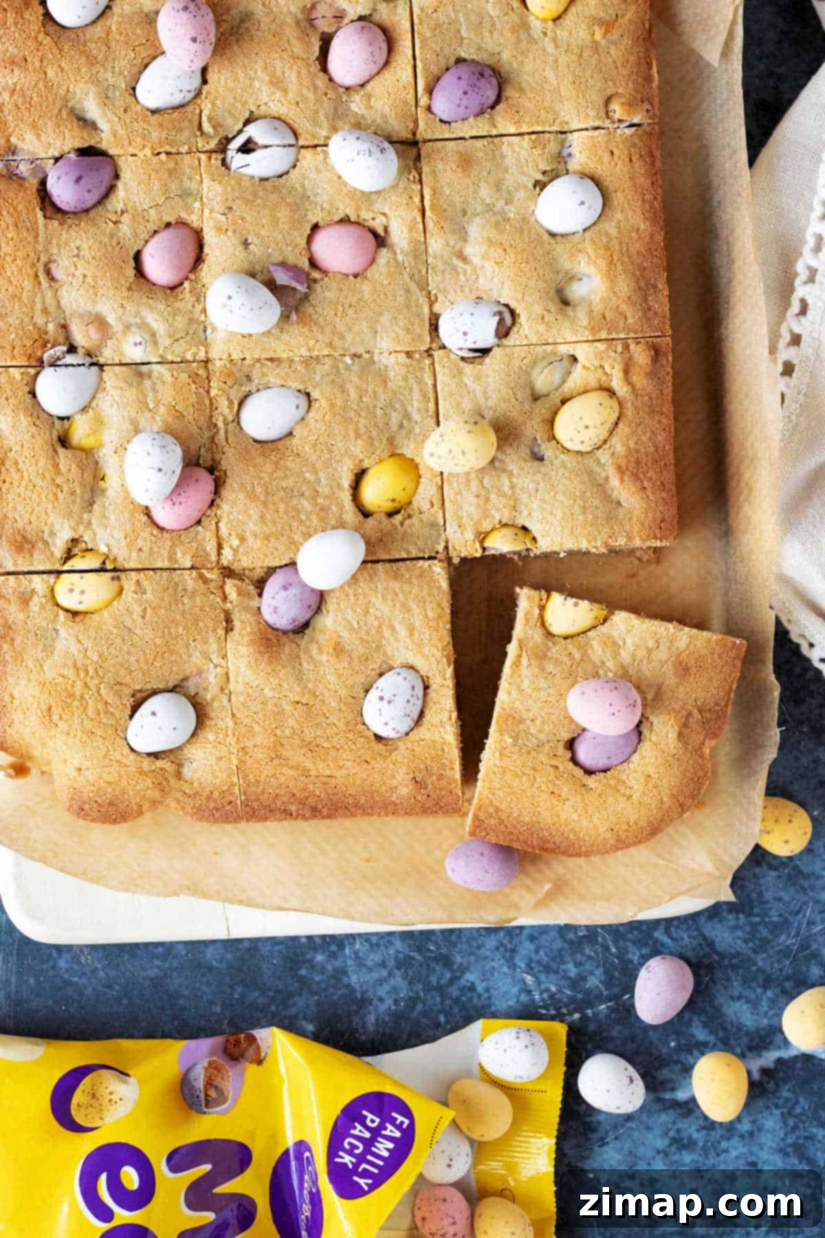 Εύκολες Μπάρες Μπισκότων Cadbury Μίνι Αυγά 2 Chocolate mini egg cookie bars cut into squares on a wooden board.