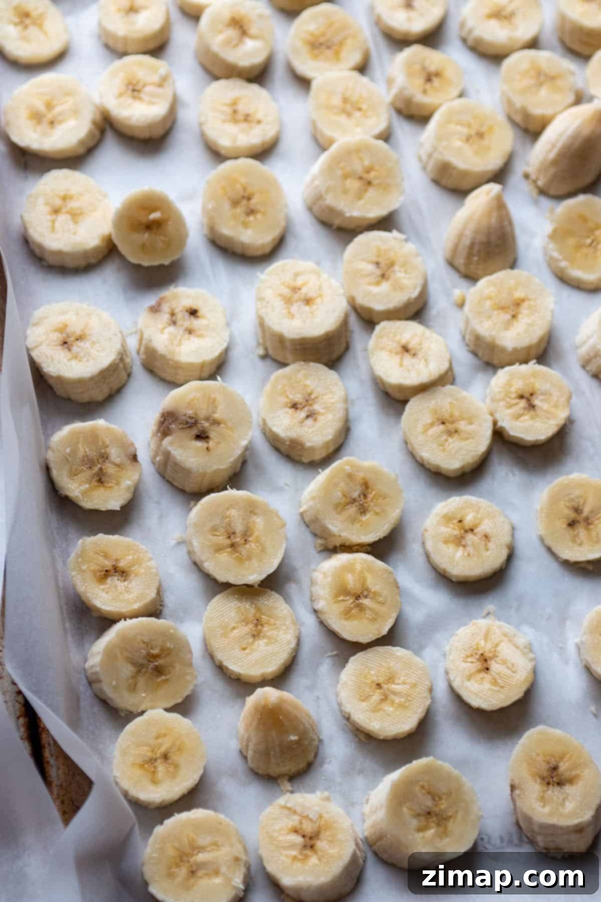 Κατάψυξη μπανάνας για smoothies 4 Ένα ταψί ψησίματος με αντικολλητικό χαρτί και κομμένες φέτες μπανάνας, τακτοποιημένες σε μία στρώση.