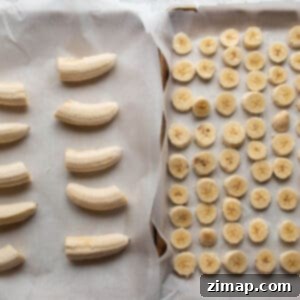 Κατάψυξη μπανάνας για smoothies 5 Δύο ταψιά στρωμένα με αντικολλητικό χαρτί, ένα με κομμένες φέτες μπανάνας και ένα με μπανάνες κομμένες στη μέση, έτοιμες για κατάψυξη.