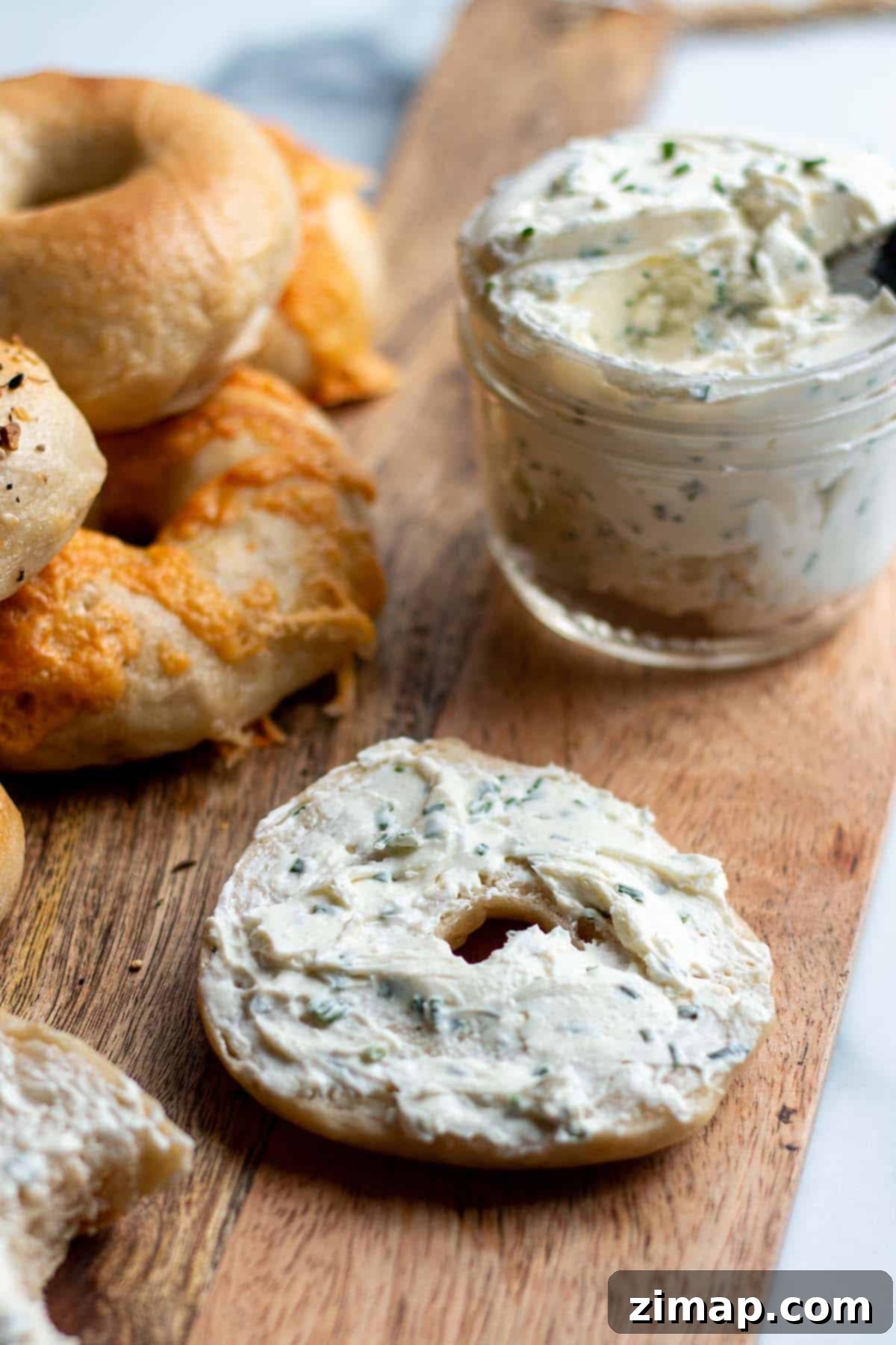 Χειροποίητα Προζυμένια Μπέιγκελ 18 Ένα bagel με τυρί κρέμα και άλλα bagels και ένα βάζο τυρί κρέμα.