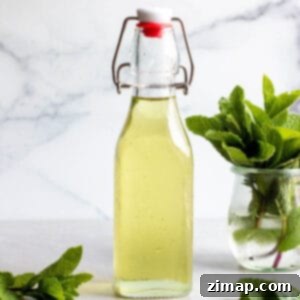 Δροσερό Σιρόπι Δυόσμου 5 Ένα γυάλινο μπουκάλι με πράσινο σιρόπι μέντας και φρέσκα φύλλα μέντας.